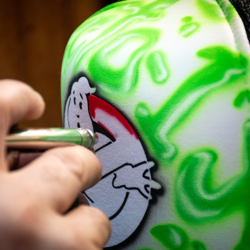 An airbrush merchandise artist painting a Ghostbusters logo on a hat