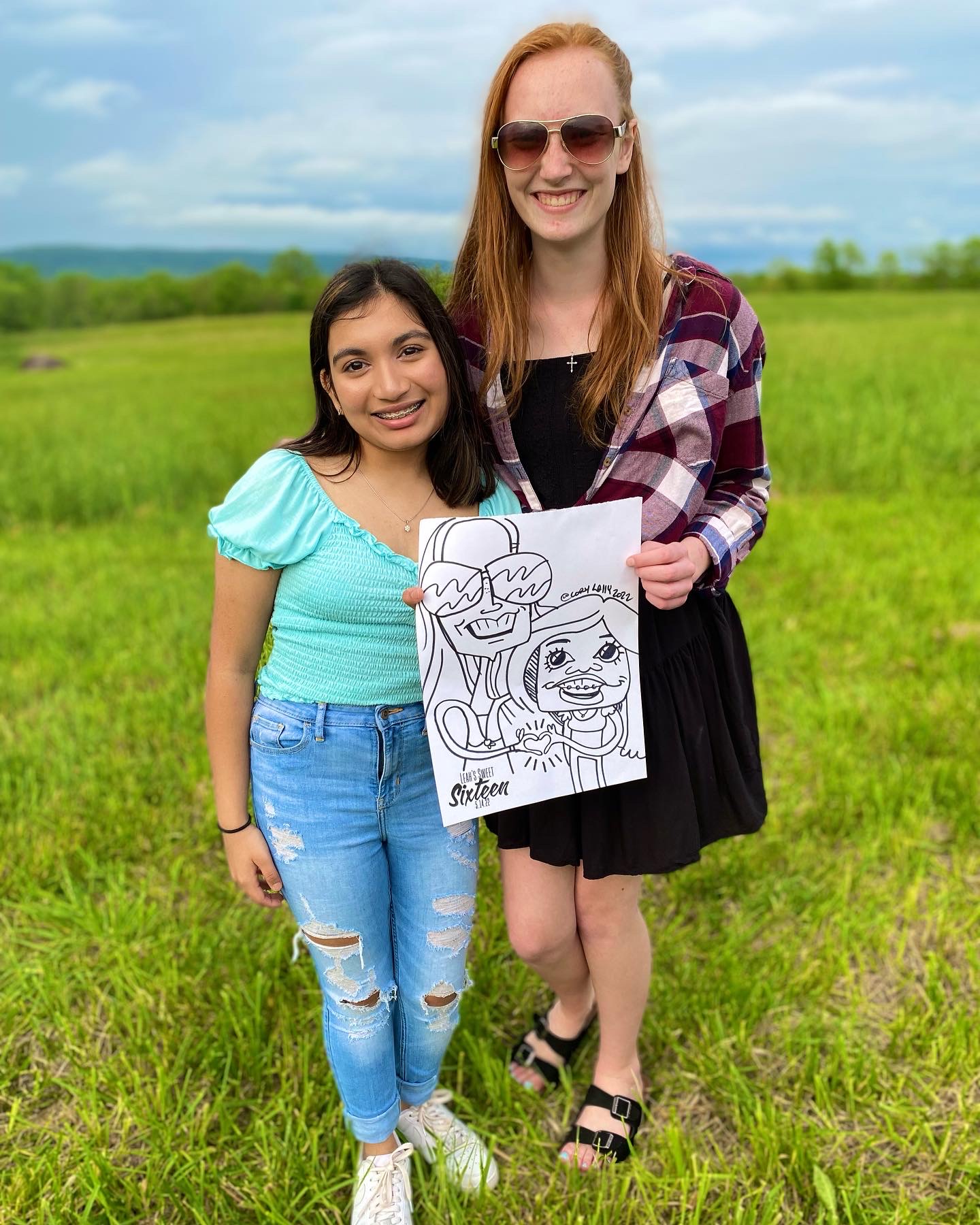 Two girls standing in a field holding a black and white caricature of themselves