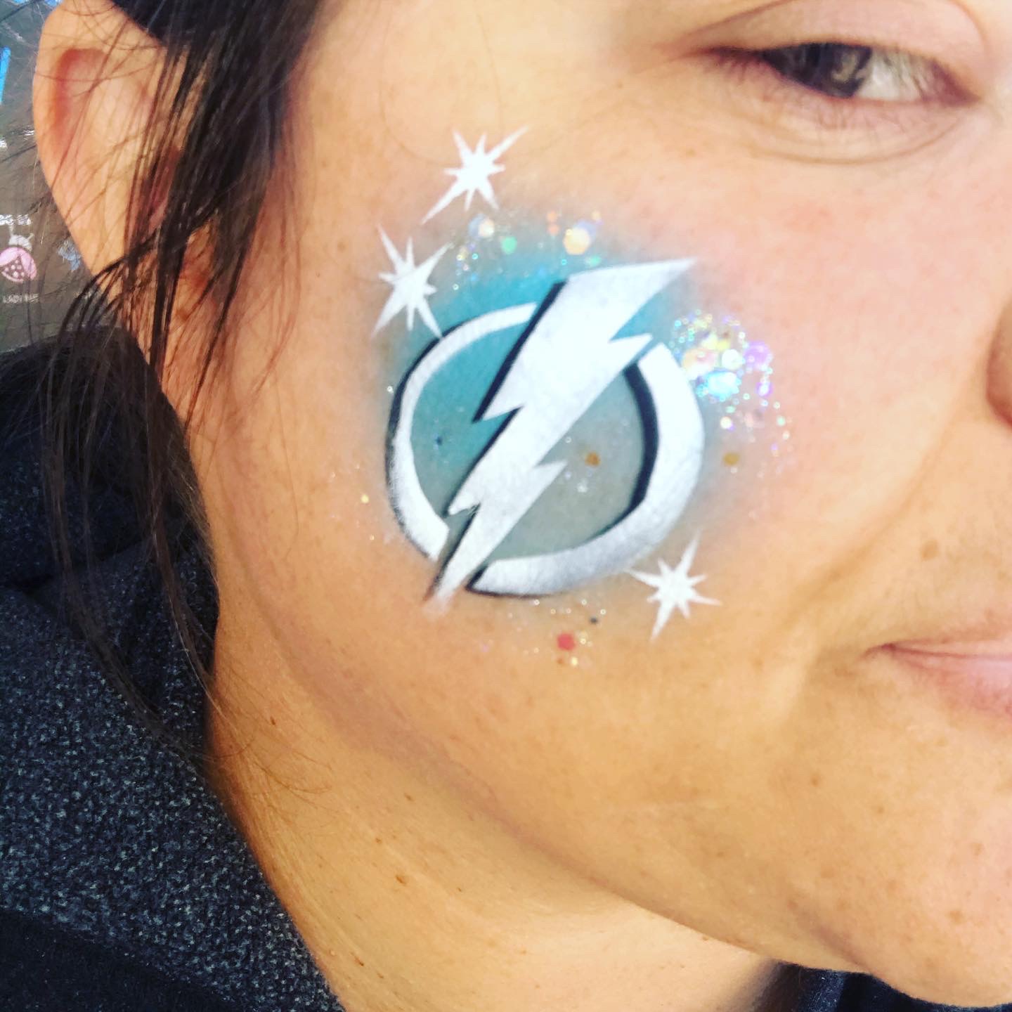 A Tampa Bay Lightning logo airbrush face paint on the cheek