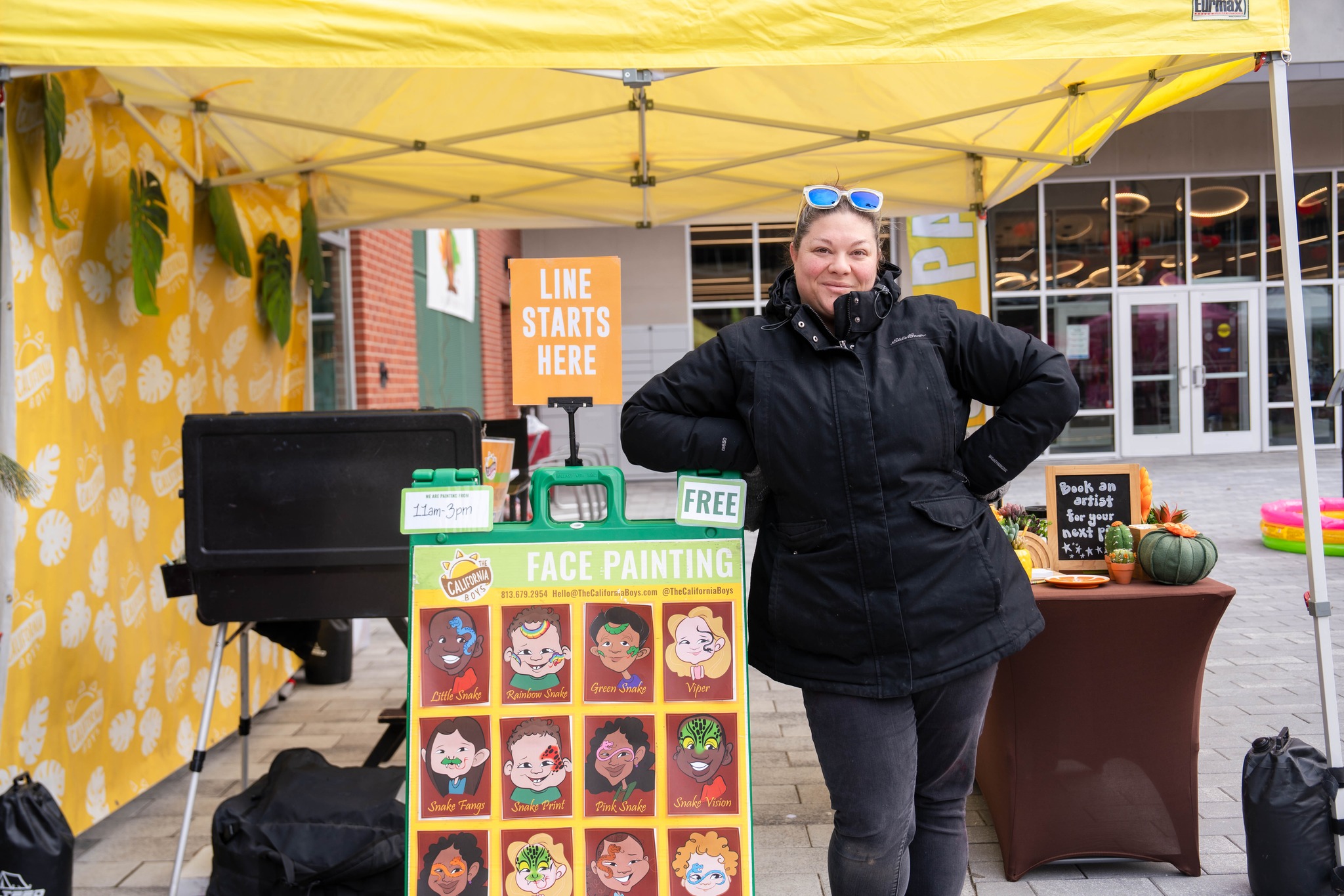 A face painter standing next to a design board inside of the tent for Lancaster Lunar New Year