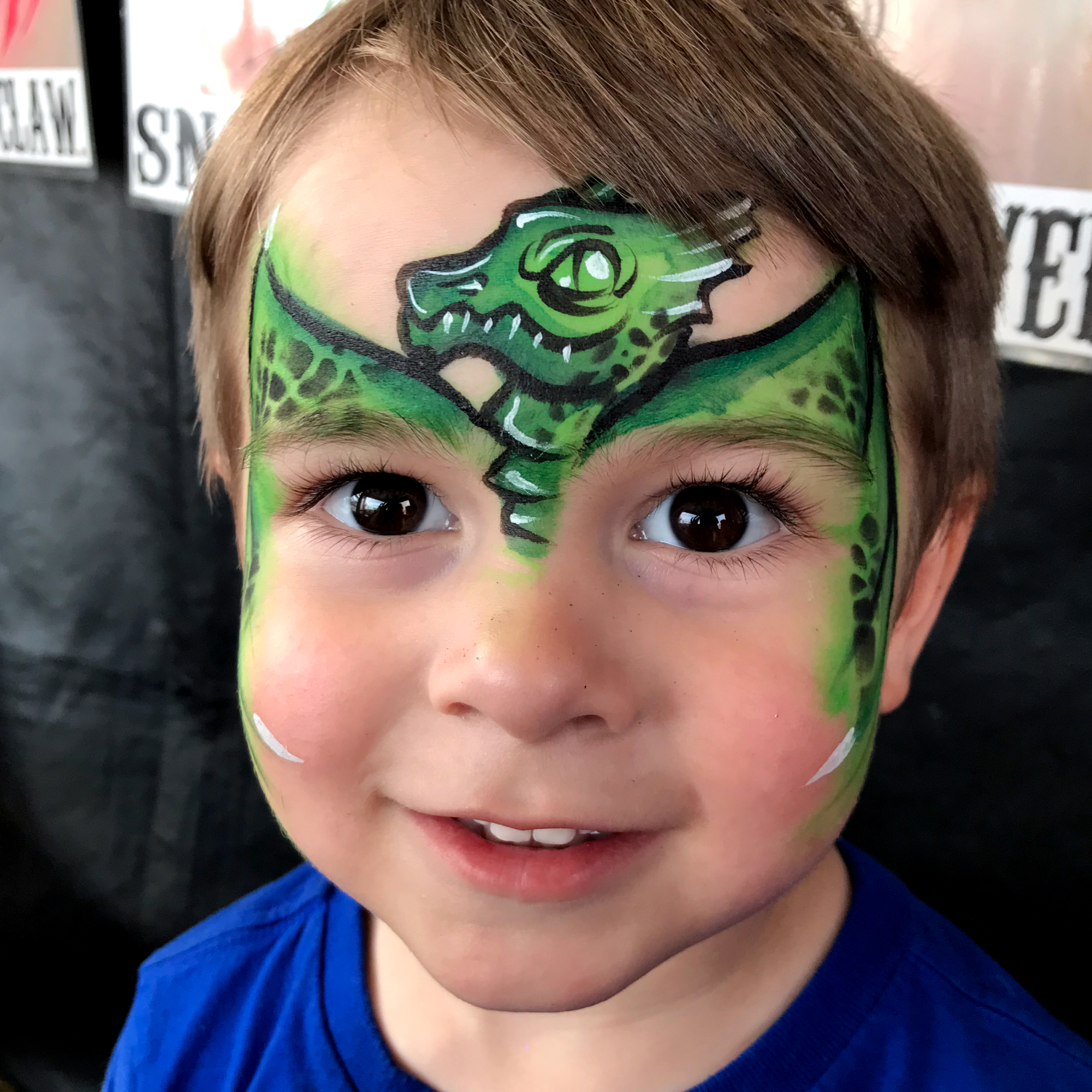 A green dragon face paint on a little boy