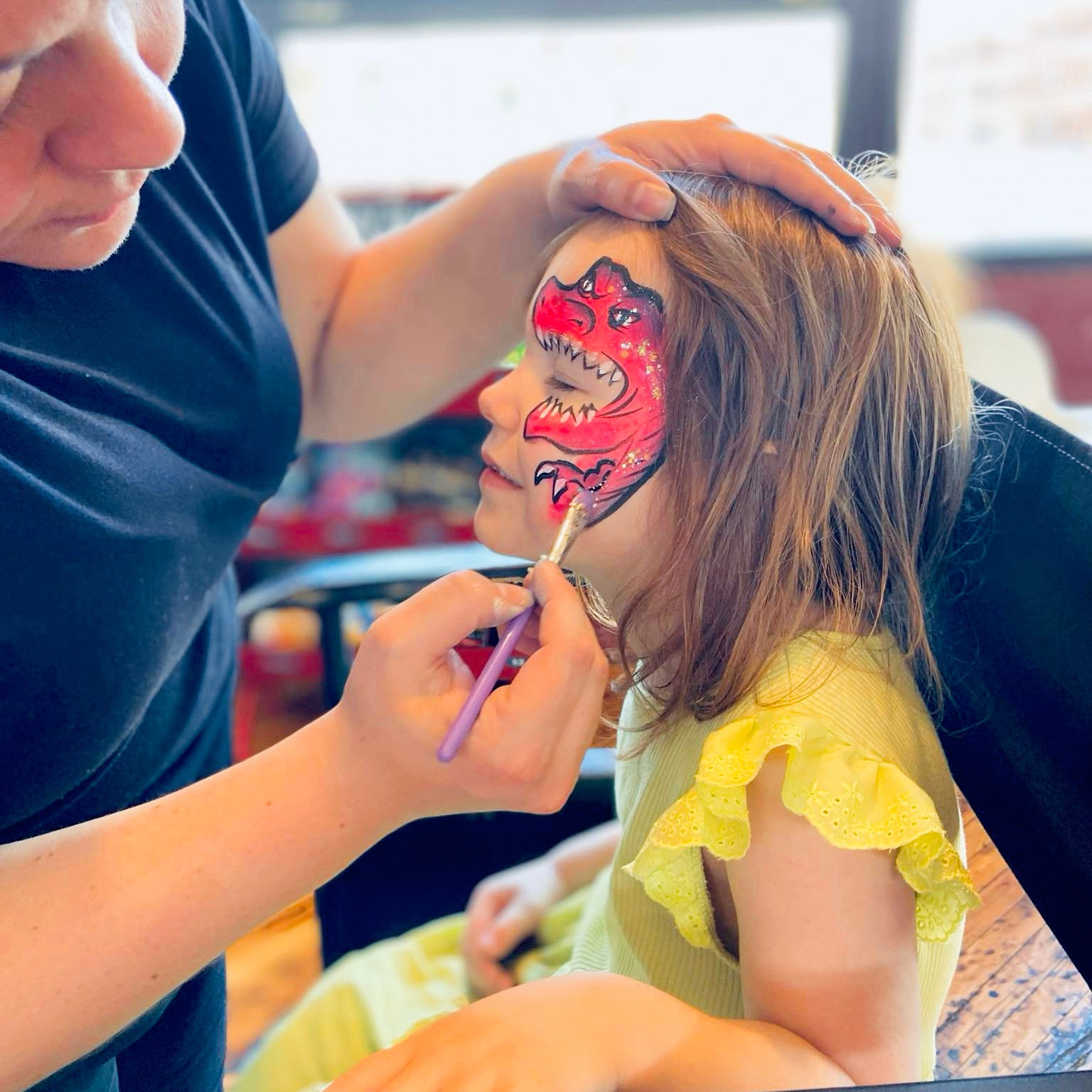 A face painter painting a trex on a little girl's face