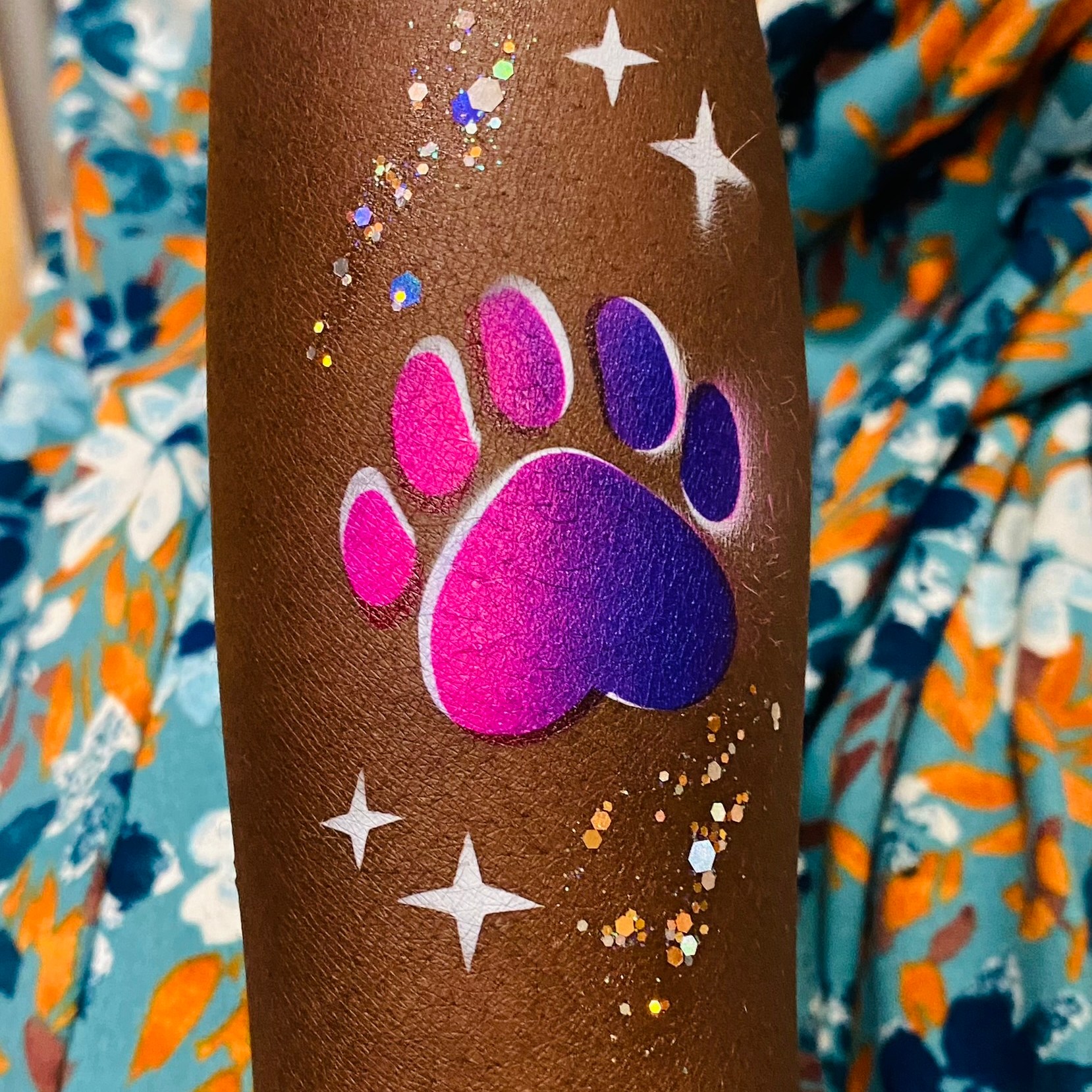 A pink and purple paw print airbrush tattoo on an arm at a school event