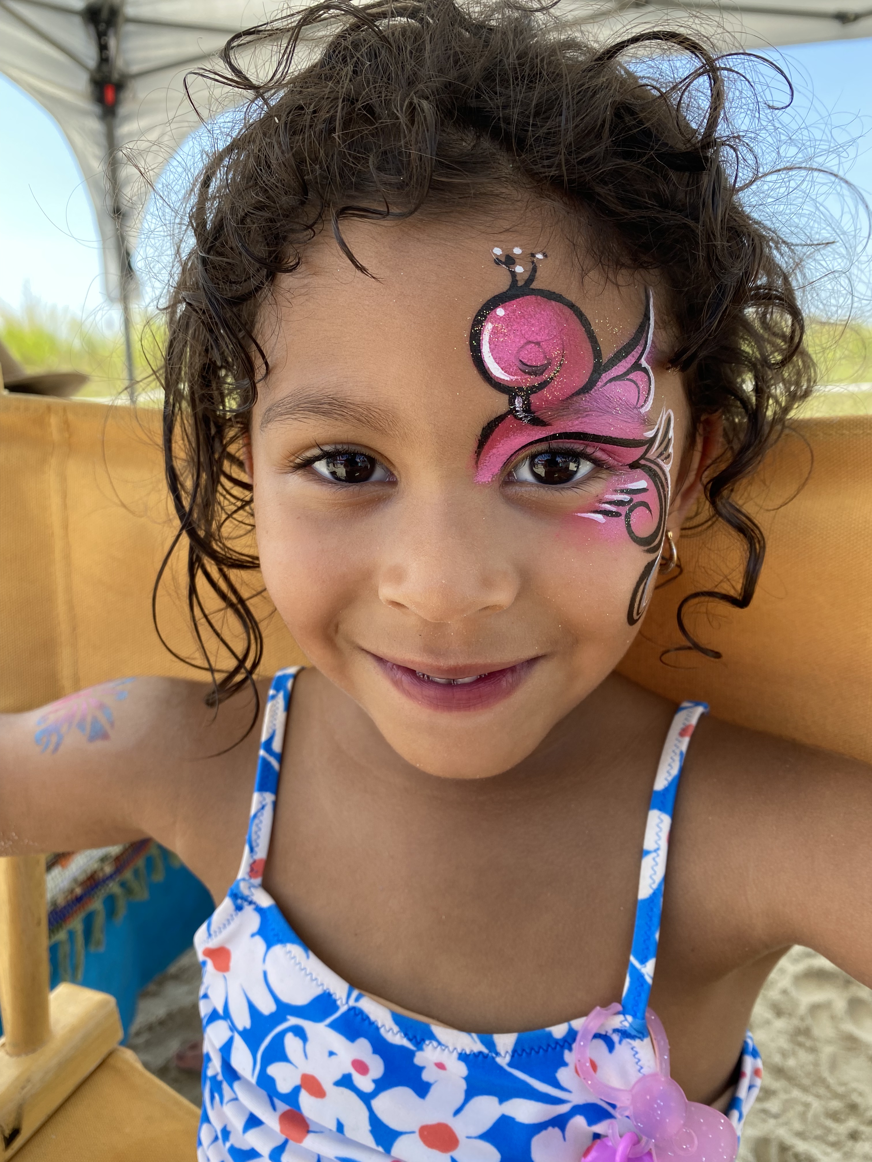 A bright pink flamingo face paint on a little girl at the beach