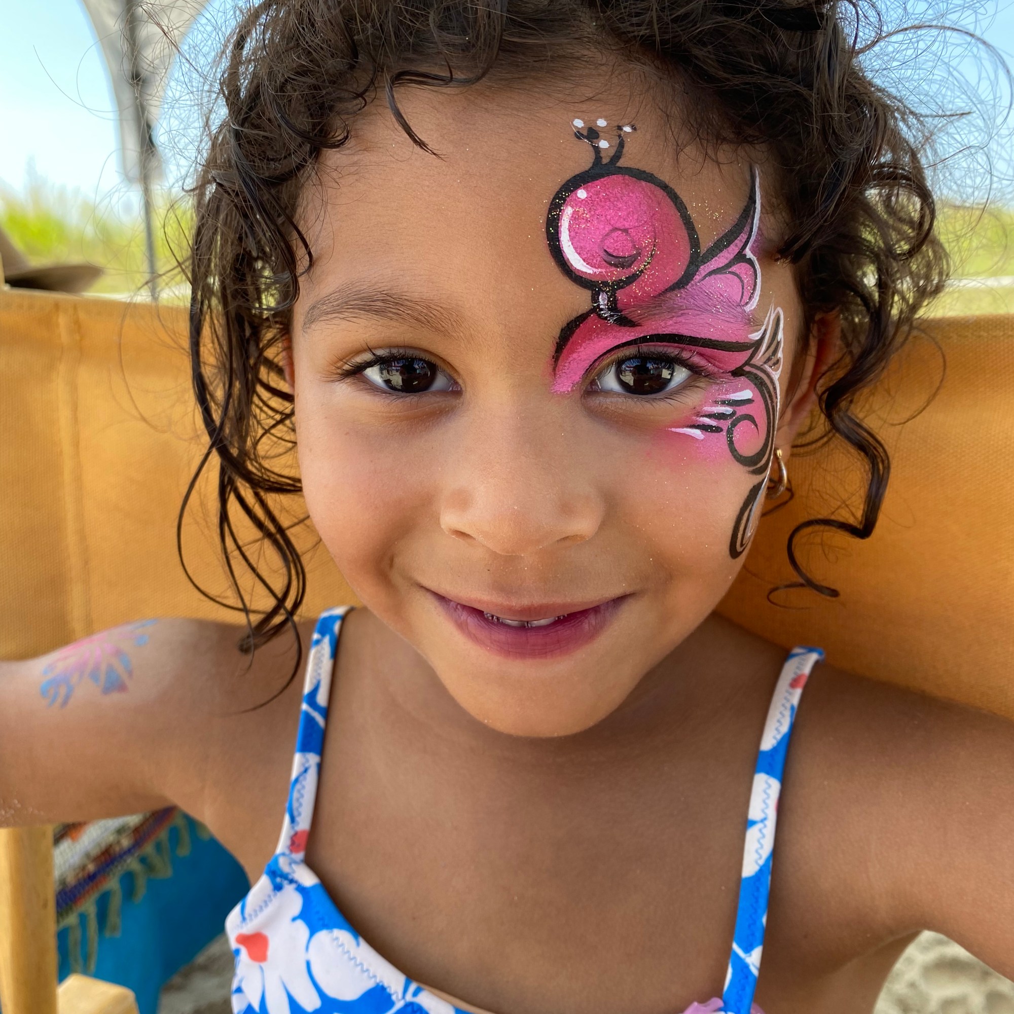 A bright pink flamingo face paint on a little girl at the beach