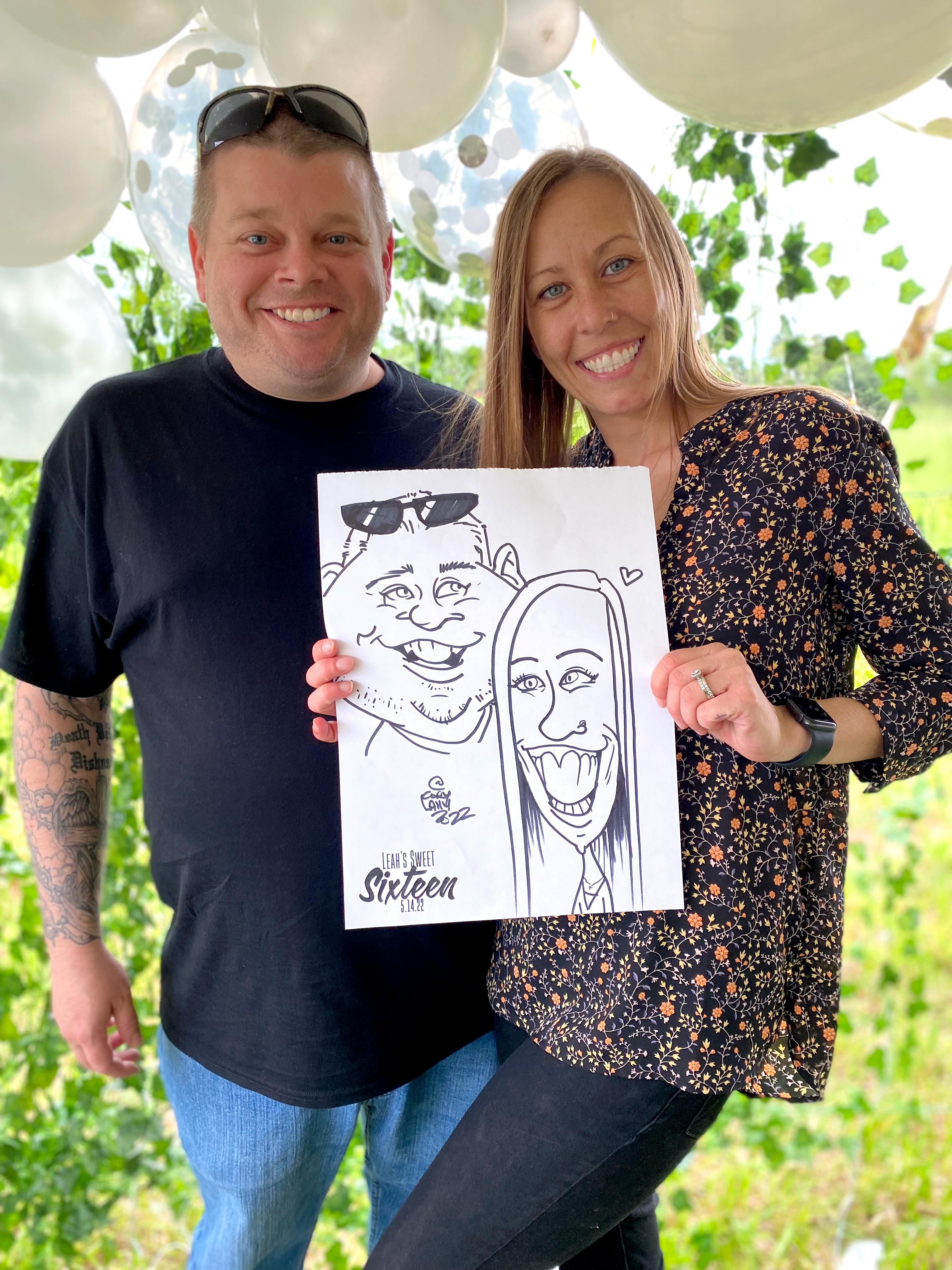 An couple posing with a black and white caricature of themselves at a summer party