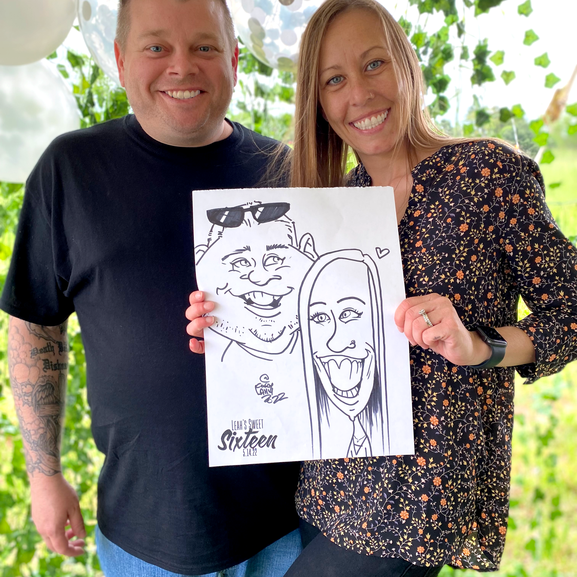 An couple posing with a black and white caricature of themselves at a summer party