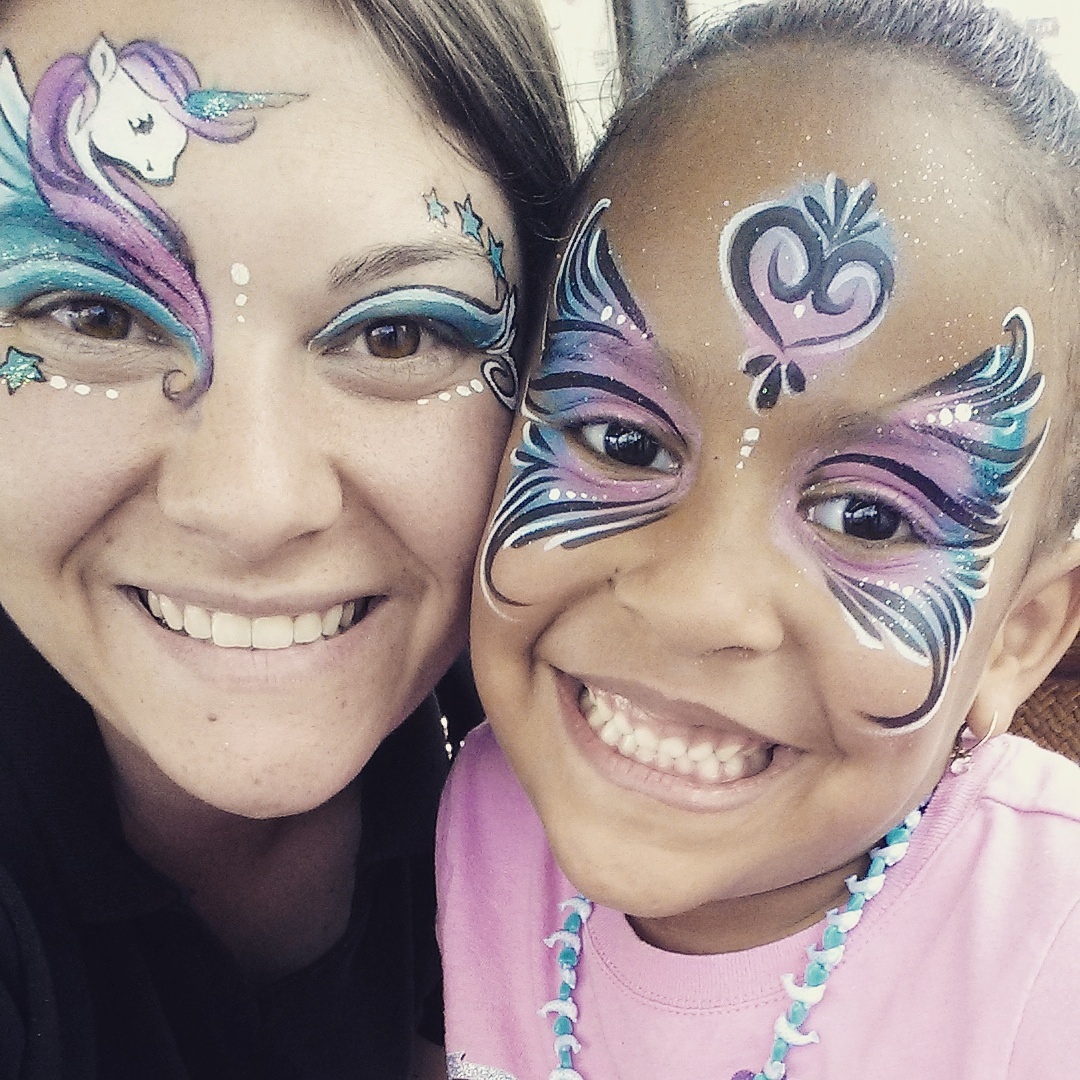 A woman with her face painted with a unicorn and a little girl with her face painted