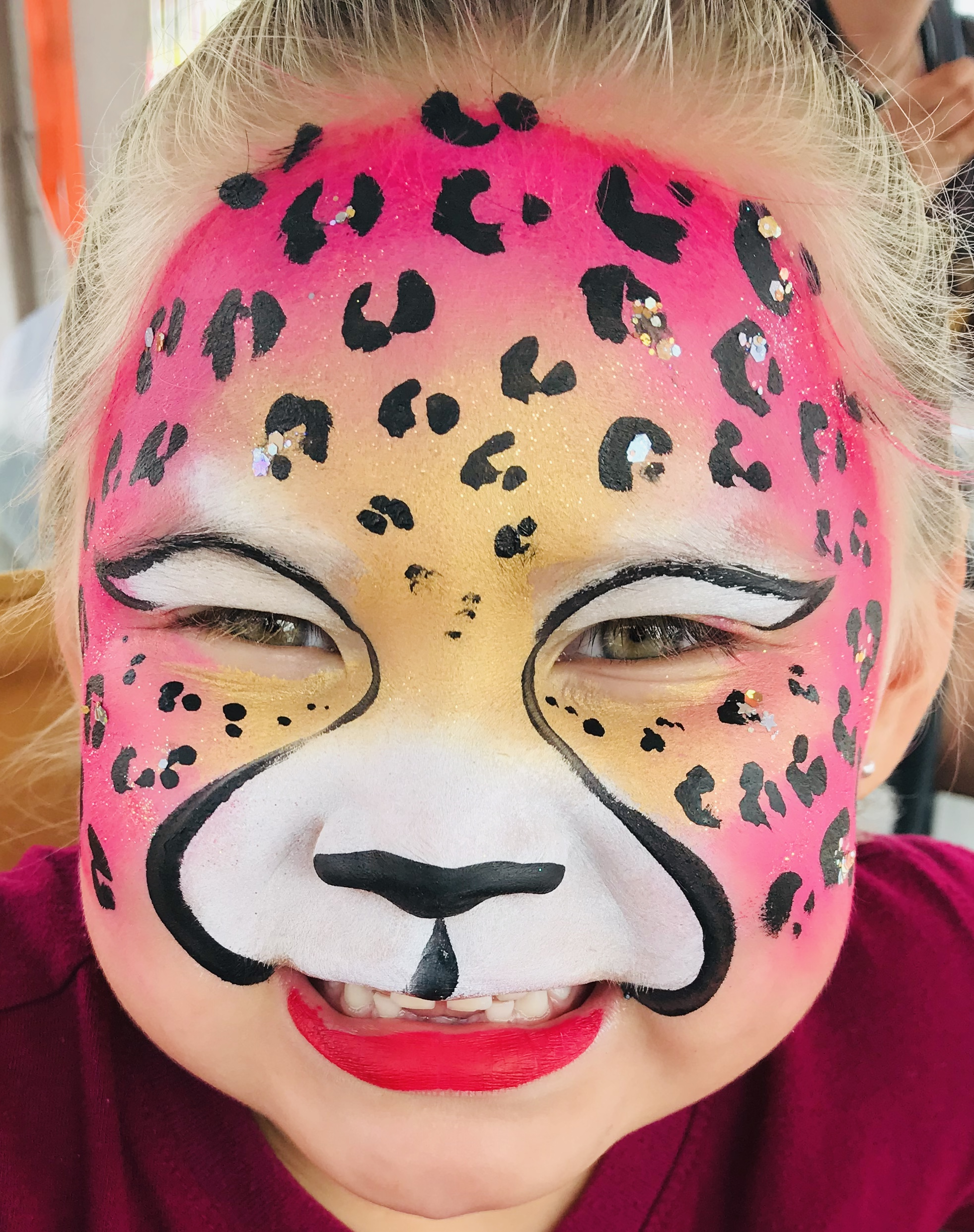 A pink and gold leopard face paint with pink lipstick