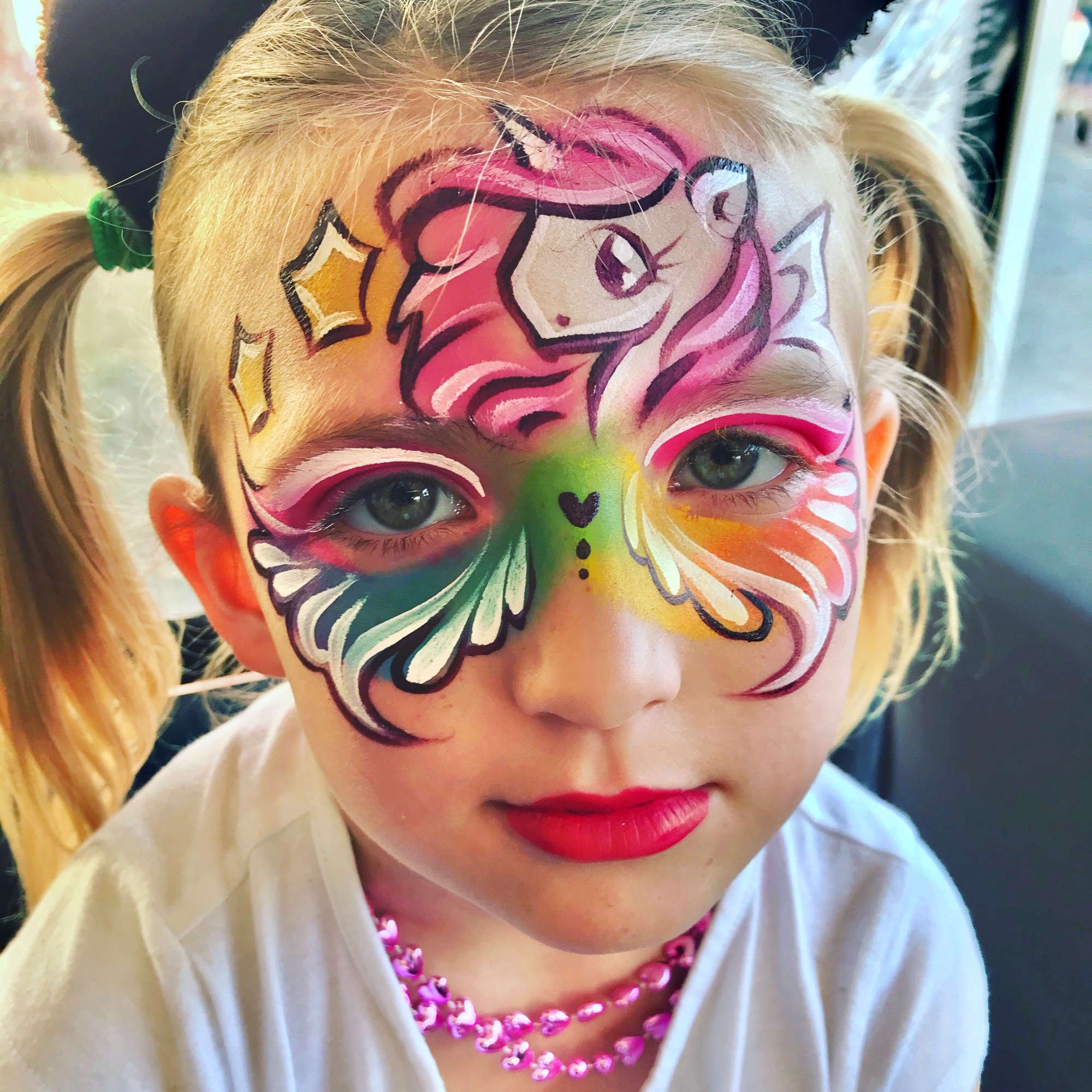 A rainbow unicorn face paint with stars on a little girl