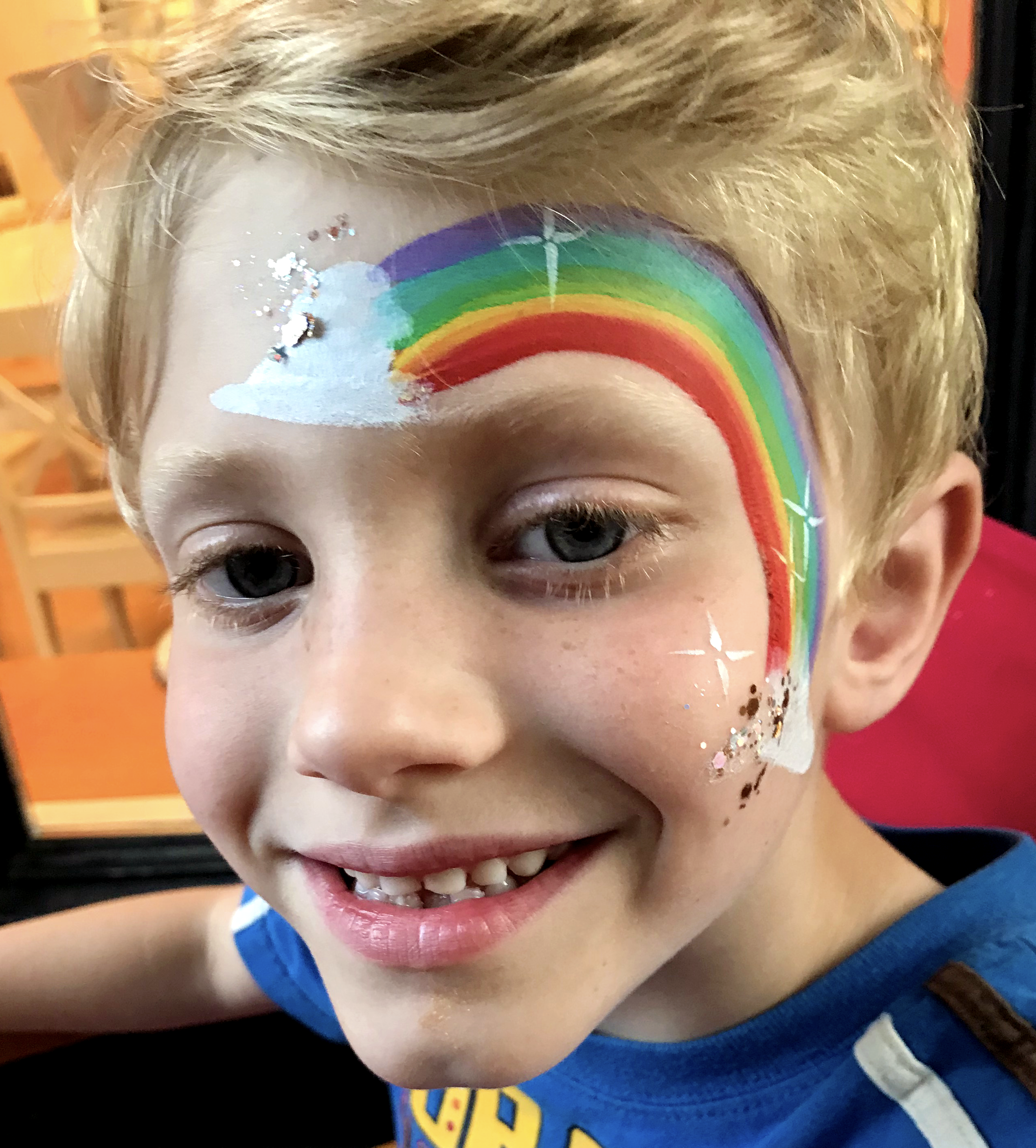 A rainbow face paint over the eye of a little boy